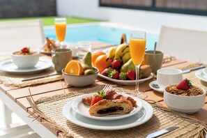 A breakfast setting with croissants, fruit, and orange juice by a poolside. - TARAZET 1 by Buenavilla | Modern townhouse with pool (Playa Blanca)