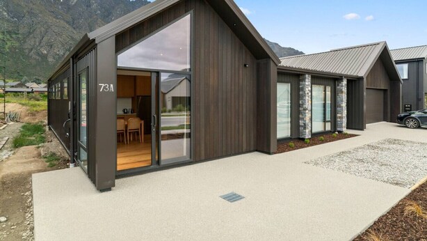 A modern house with a large glass door entrance, a kitchen visible inside, and a driveway leading to a parked car. - Luxury Stay Next To Iconic Remarkables Mountains (Jacks Point)