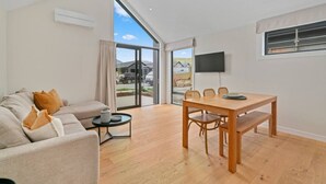 A modern living room with a sofa, a dining table with chairs, a TV mounted on the wall, and a large window with a view of the outside. - Luxury Stay Next To Iconic Remarkables Mountains (Jacks Point)