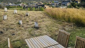 A wooden table and chairs in a grassy area with a view of mountains and modern houses. - Luxury Stay Next To Iconic Remarkables Mountains (Jacks Point)