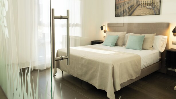Una habitación de hotel con cama, mesitas de noche, un cuadro en la pared y una ventana con cortinas.