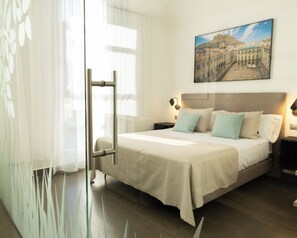 Una habitación de hotel con cama, mesitas de noche, un cuadro en la pared y una ventana con cortinas.