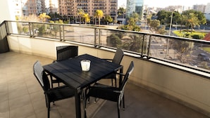 Un balcón con mesa y sillas, con vista a un paisaje urbano con edificios y palmeras.