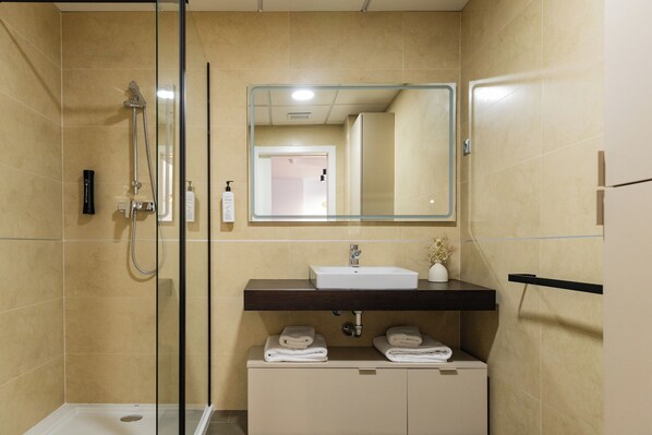 A modern bathroom with a glass-enclosed shower, a sink with a dark countertop, and a mirror above it. - Guillman Suites (Alicante)