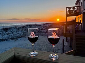 Dos copas de vino con personajes de dibujos animados en una terraza de madera con vistas a una playa al atardecer.
