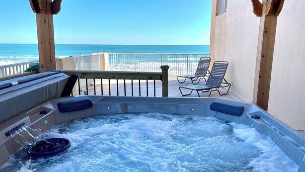 Un jacuzzi con vista al océano, terraza de madera y sillas de descanso.