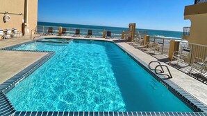 Una piscina con agua cristalina azul, rodeada de sillas de descanso y vista al océano.