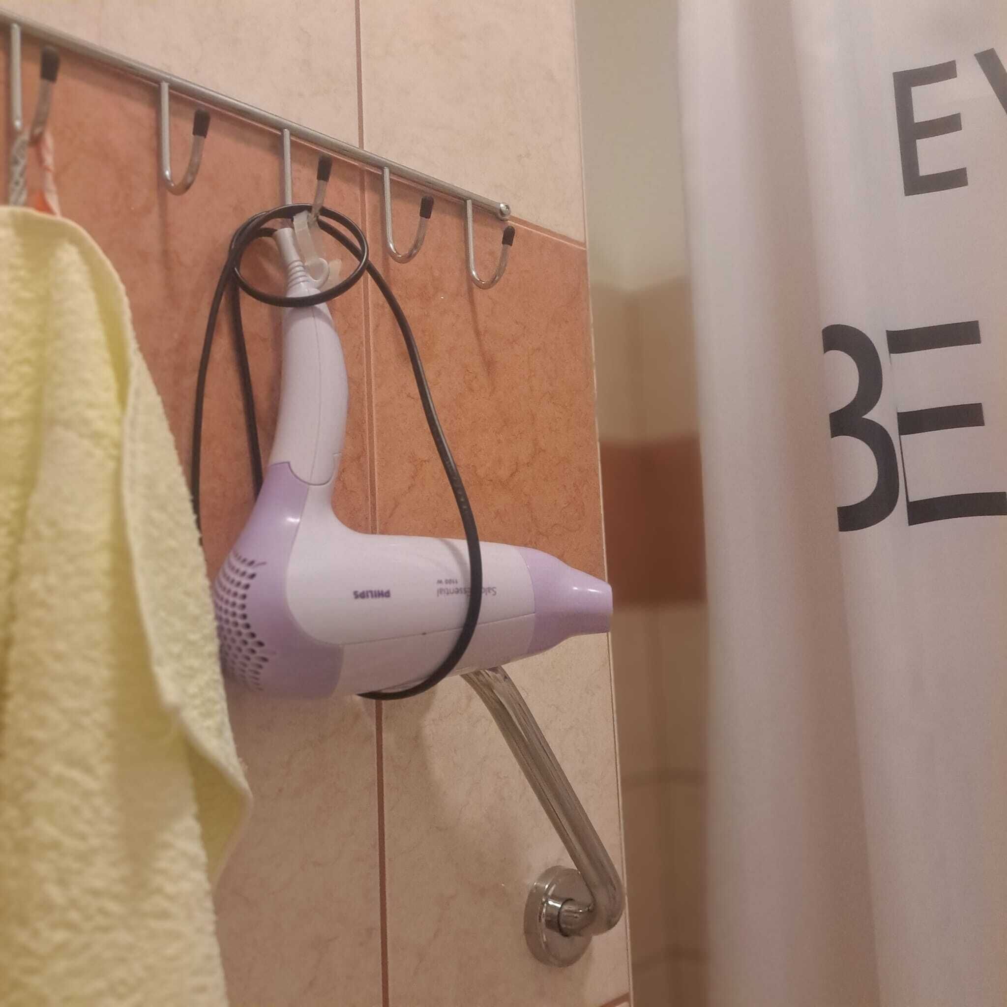 Un baño con un secador de pelo montado en la pared, un perchero y una cortina de ducha con texto.