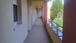 A corridor with a tiled floor, a window with blinds, and a balcony with a metal railing. - Apartment Golf in  the Spa of Bük, near thermal baths and golf course (Bük)