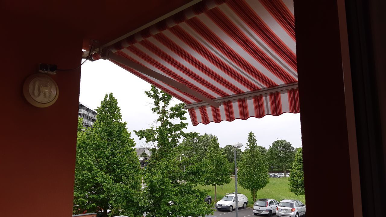A view from a covered outdoor area with a striped awning, a street lamp, and parked cars in the background.