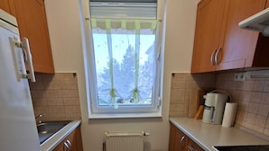 A kitchen with wooden cabinets, a white refrigerator, a stove, a window with a curtain, and a radiator. - Apartment Golf in  the Spa of Bük, near thermal baths and golf course (Bük)