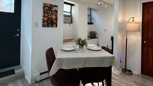 A dining area with a table set for two, a potted plant, and a painting on the wall.
