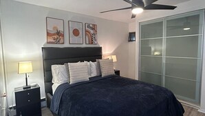 A bedroom with a bed, a nightstand, a ceiling fan, and a sliding glass door.