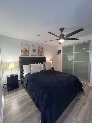 Un dormitorio con cama, mesita de noche, ventilador de techo y puerta corrediza de vidrio.