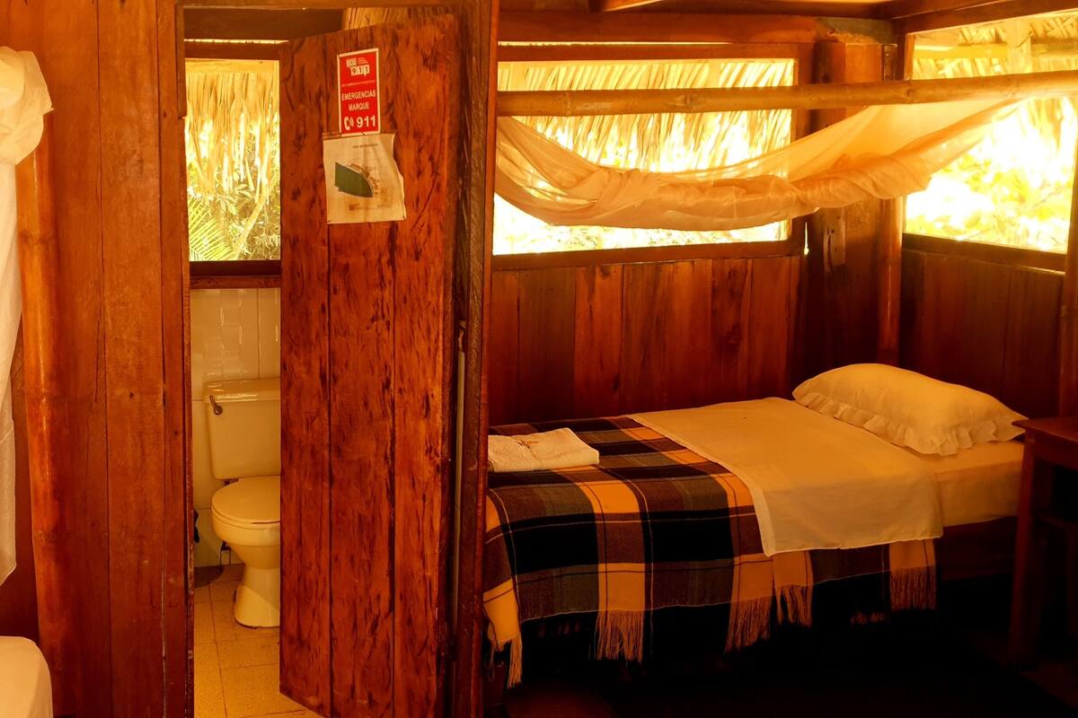 Une chambre dans un chalet en bois, équipée d’un lit, de toilettes et d’un lit à baldaquin.