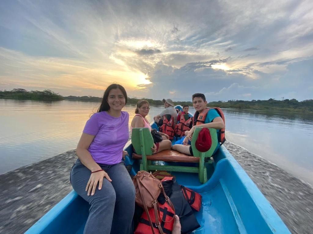 A group of people in a blue boat on a calm body of water during sunset.