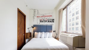 A bedroom with a bed, a headboard, a wall mural, a window, and a radiator. - Cozy Hotel in Soho, Standard Queen Room (New York)