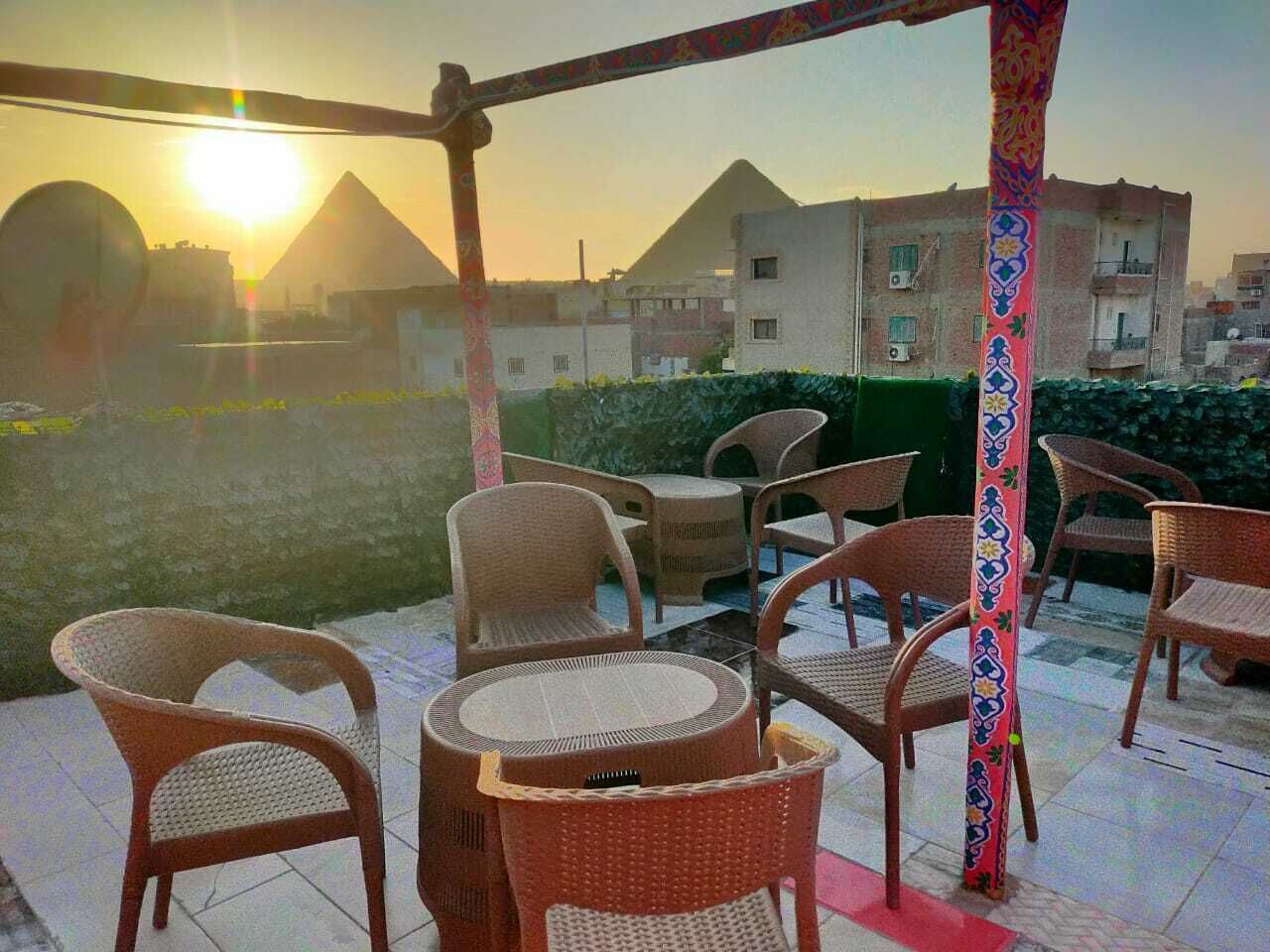 An outdoor seating area with wicker chairs and a table, overlooking a cityscape with buildings and a pyramid silhouette against the sunset.