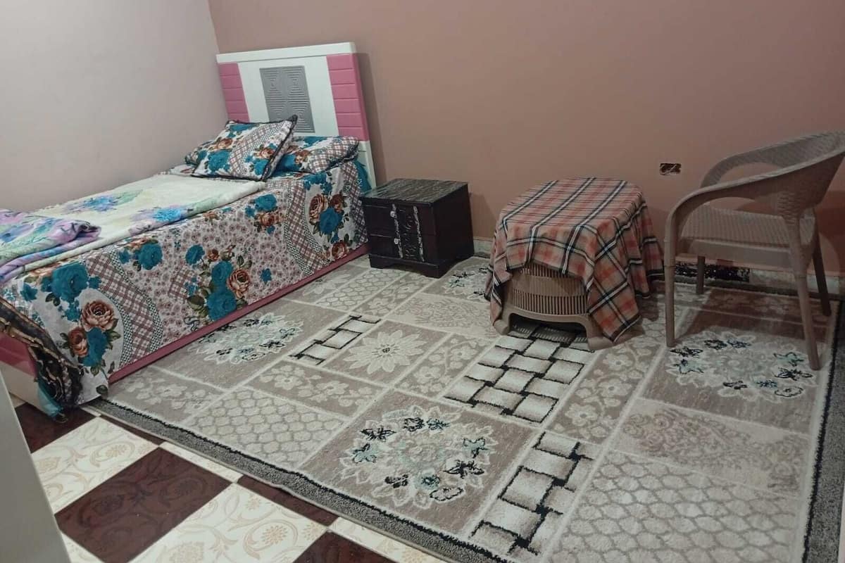A bedroom with a bed, a small table, a chair, and a rug.