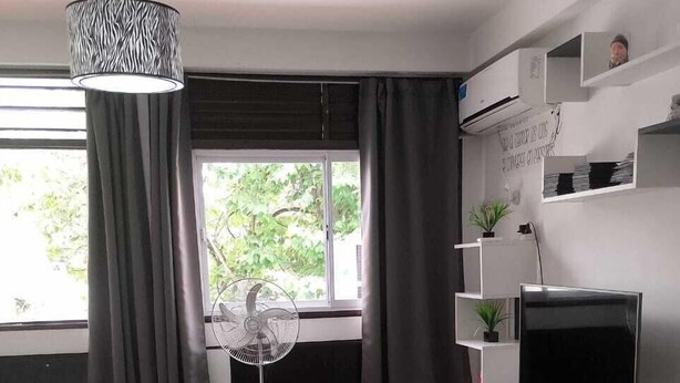A modern hotel room with a bed, a standing fan, a TV, and a window with curtains. - SHADDAI ALOJAMIENTOS (Salta)