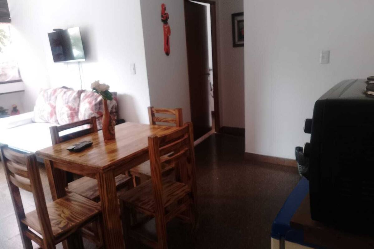 Ein Essbereich mit Holztisch und Stühlen, einer Vase mit Blumen und einem Fernseher an der Wand.