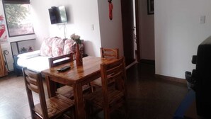 A dining area with a wooden table and chairs, a vase with flowers, a television on the wall, and a door leading to another room. - SHADDAI ALOJAMIENTOS (Salta)
