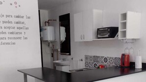A modern kitchen with white cabinets, a black countertop, and a bar stool. - SHADDAI ALOJAMIENTOS (Salta)