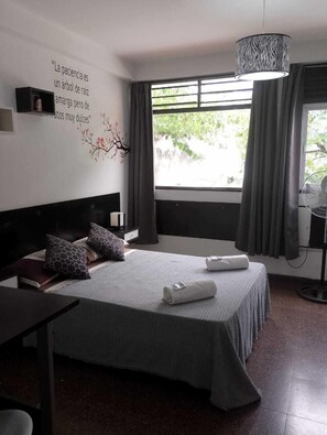 A modern hotel room with a large bed, a bedside table, a wall-mounted shelf, a window with curtains, and a ceiling fan. - SHADDAI ALOJAMIENTOS (Salta)