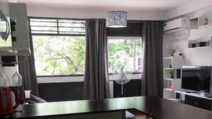 A modern kitchen with a sink, a coffee maker, and a fan. There is a window with curtains and a view of greenery outside. - SHADDAI ALOJAMIENTOS (Salta)