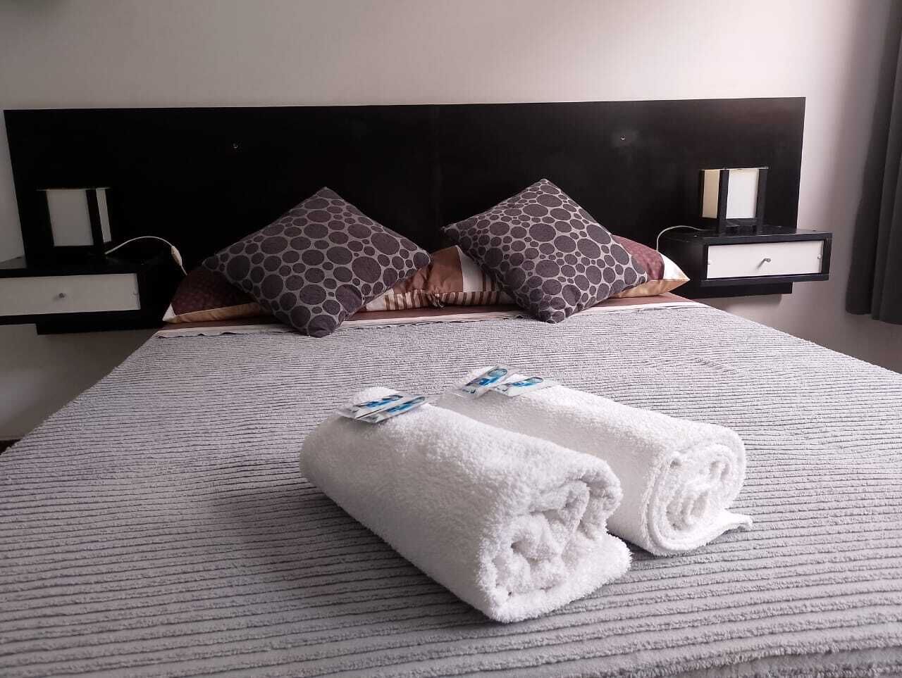 A neatly made bed with a striped bedspread, two rolled white towels, and patterned pillows.