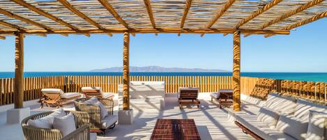 Een strandlounge met rieten meubilair, een houten tafel en uitzicht op de oceaan.