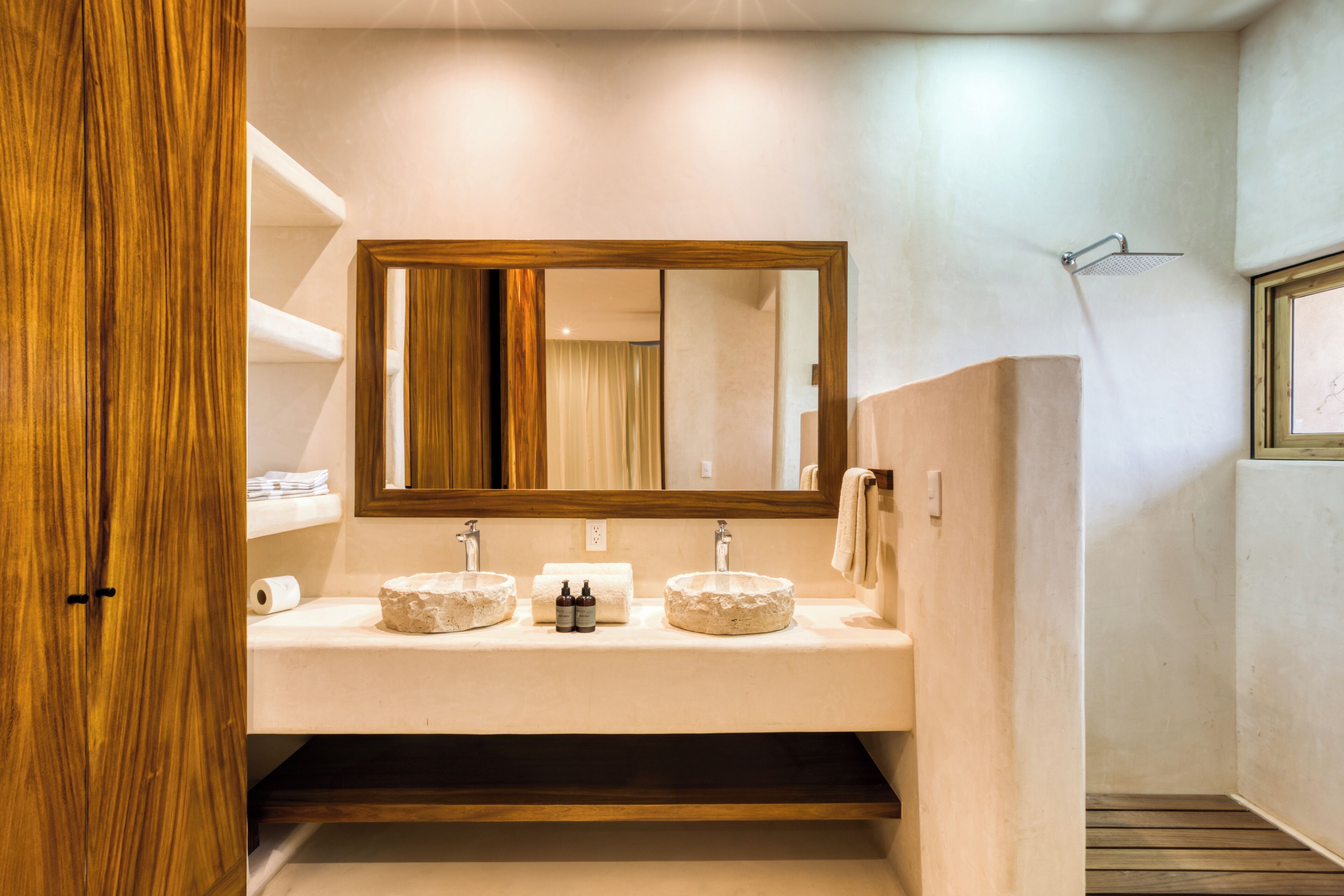 Un baño con tocador de madera, dos lavamanos, un espejo grande y una ducha.