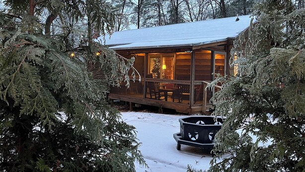Una cabaña con porche, rodeada de árboles cubiertos de nieve.