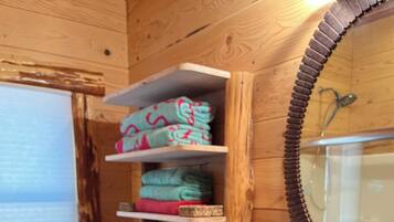 A wooden cabin bathroom with a toilet, shelves with folded towels, a sink with a black basin, and a stone backsplash.