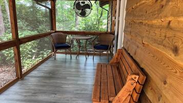 A wooden deck with a bench and two wicker chairs with cushions, overlooking a forested area.
