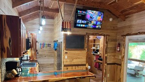 Interior rústico de una cabaña con una zona de bar de madera, un televisor montado en la pared y techo de madera.