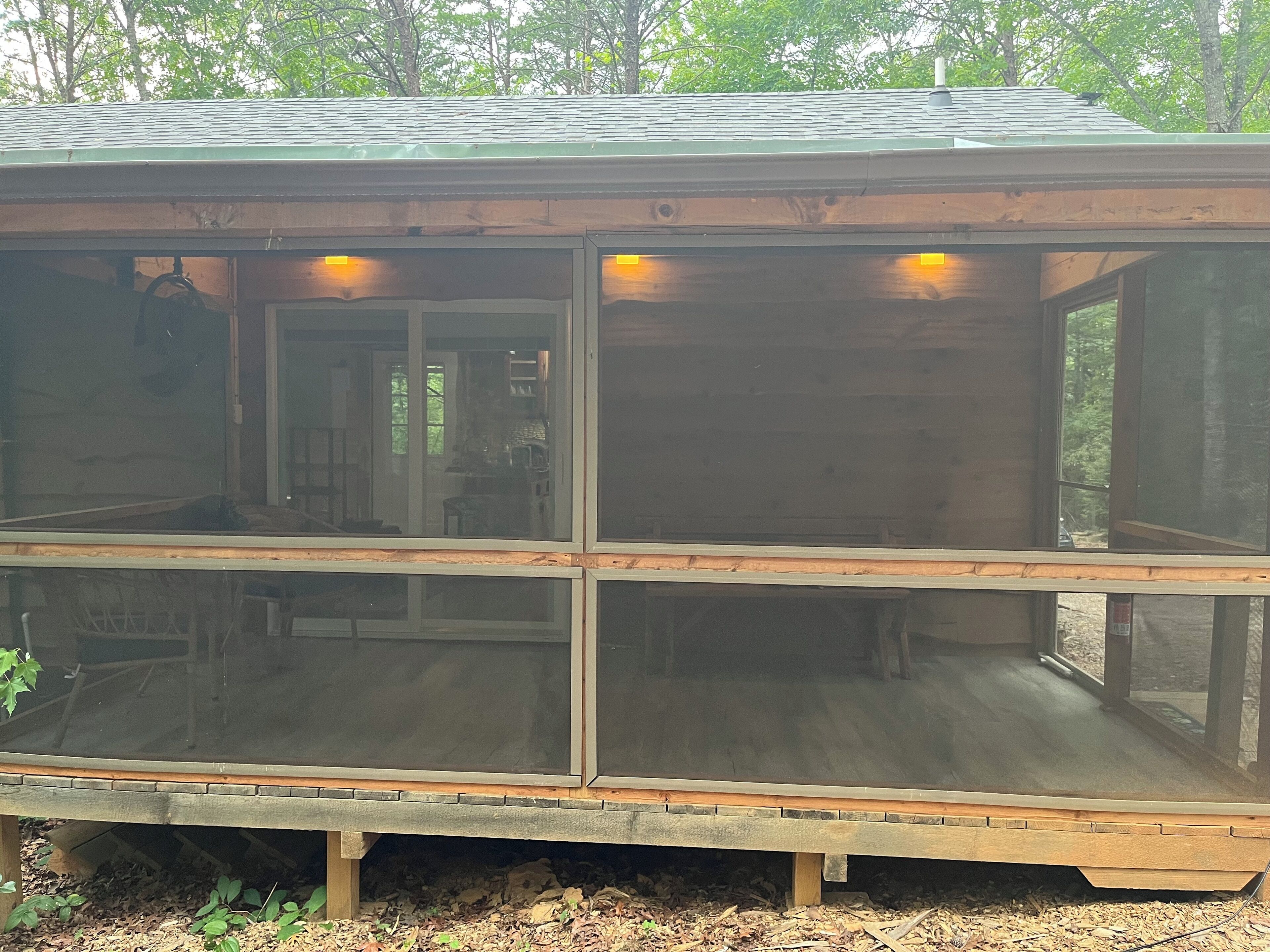 Eine Holzhütte mit einer überdachten Veranda, großen Fenstern und einem einsehbaren Innenraum mit Essbereich.
