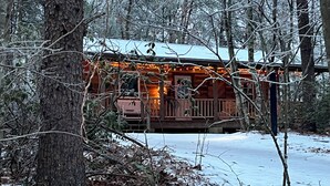 Una cabaña con terraza de madera y suelo cubierto de nieve.