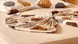 Una cama con colchón color beige, almohadas con diseños geométricos y una manta doblada con un estampado marrón y blanco.