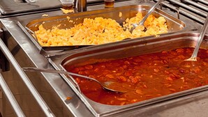 Un bufé con diversas opciones de comida, como huevos revueltos, frijoles y salsa roja.