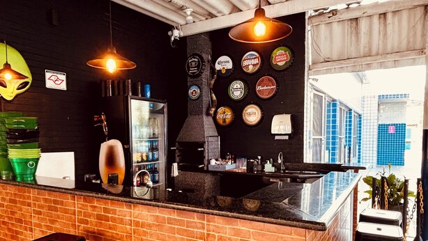 Zona de bar con mostrador de ladrillo, taburetes negros y luces colgantes.