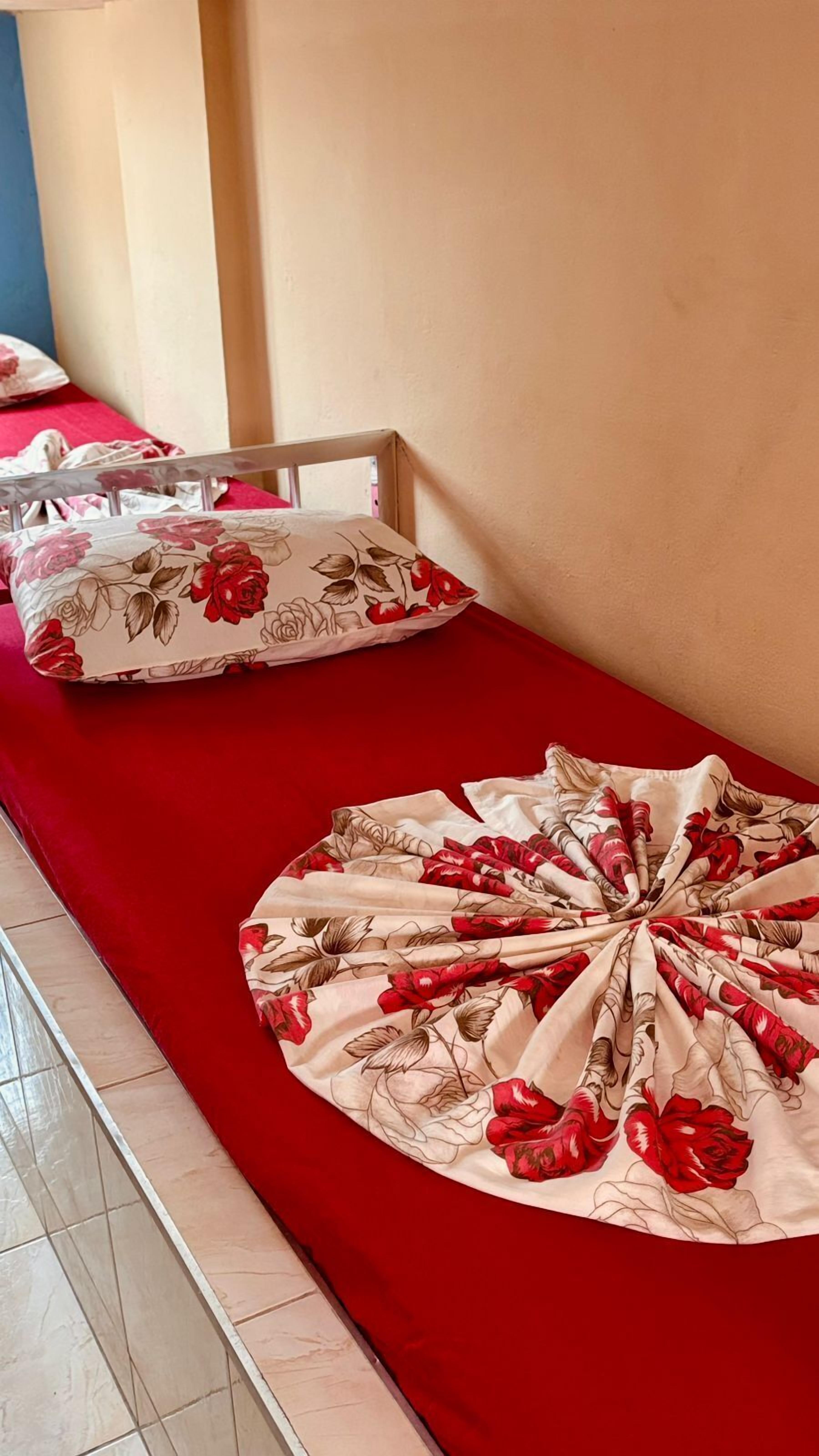 A bed with a red bedspread and floral pillows.