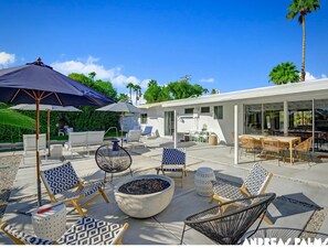 Eine moderne Außenpatio mit Lounge-Möbeln, einem Feuerkorb und Sonnenschirmen.