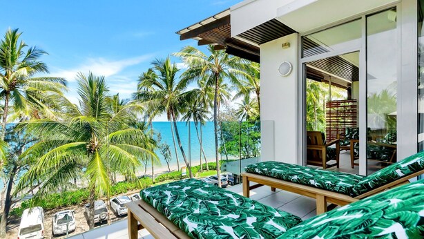 Eine moderne Villa mit Balkon und Blick auf Strand, Palmen und das Meer.
