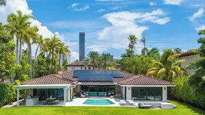 A modern house with a swimming pool, a covered patio, and a view of a tall building. - Sunset 4BR Waterfront Villa in Golden Isles w/ Heated Pool & Spa (Hallandale Beach)