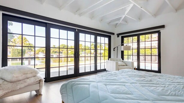 A spacious bedroom with large windows, a white bed, and a white chair. - Sunset 4BR Waterfront Villa in Golden Isles w/ Heated Pool & Spa (Hallandale Beach)