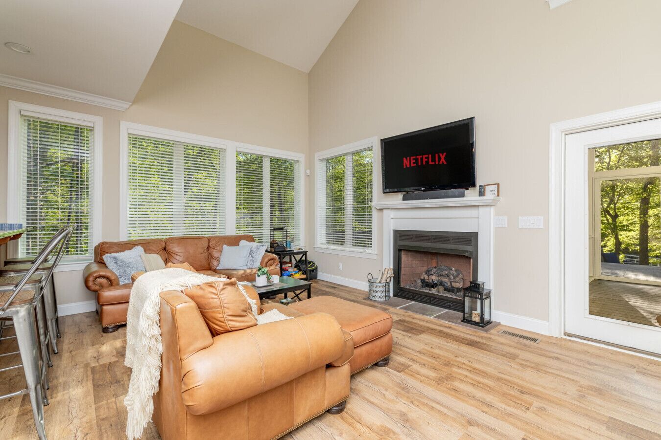 A spacious living room with a fireplace, a leather sofa, and a TV mounted above it.