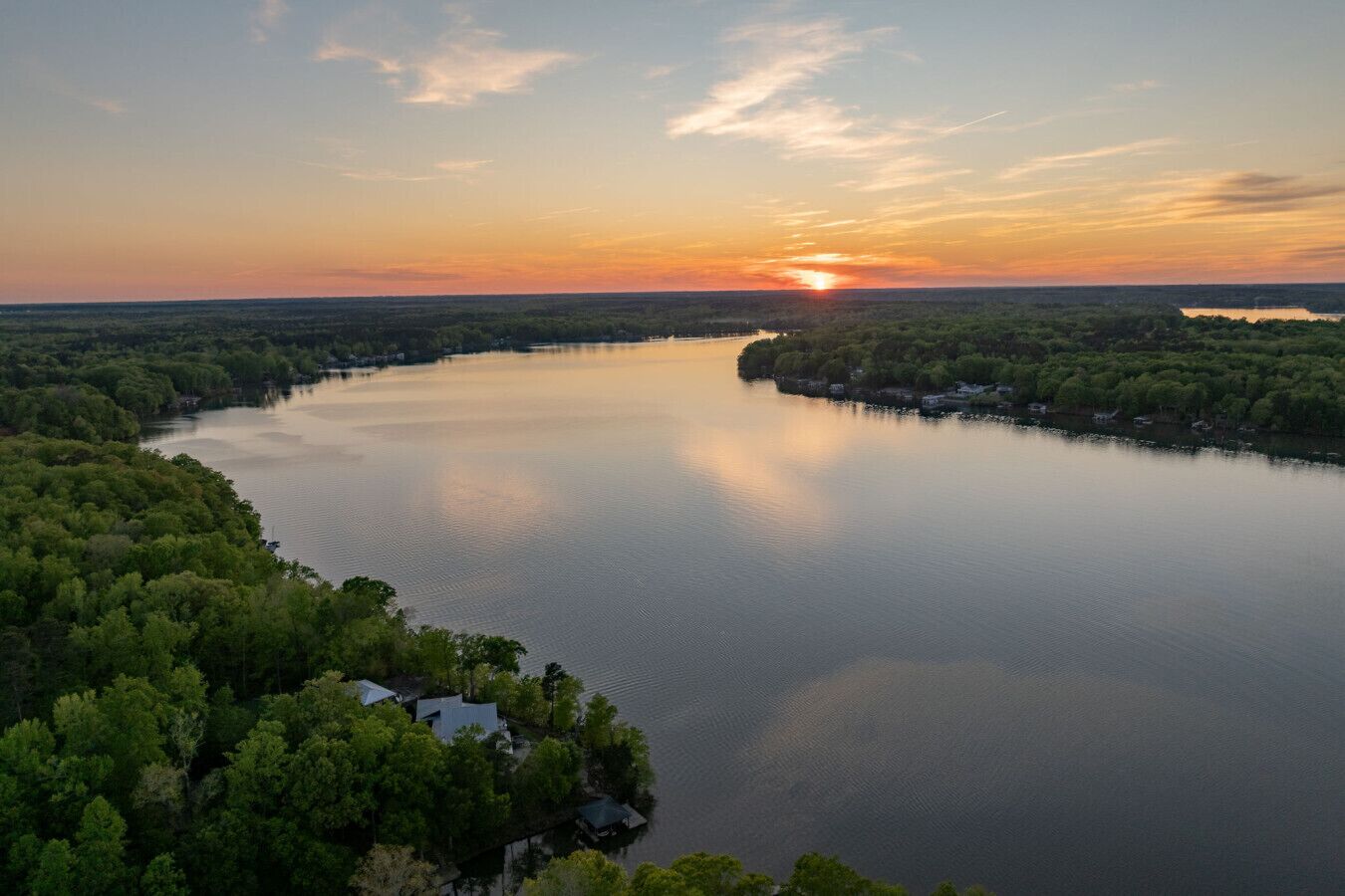 Een rivier omgeven door dicht bos, met een zonsondergang op de achtergrond.