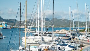 A marina with multiple sailboats docked, a large ship with a colorful design, and a mountainous backdrop. - Mobiretreat by Klodge - waterfront design flat (Olbia)