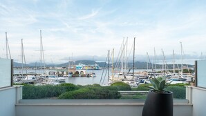 A balcony with a potted plant, overlooking a marina with numerous sailboats and a colorful boat in the background. - Mobiretreat by Klodge - waterfront design flat (Olbia)
